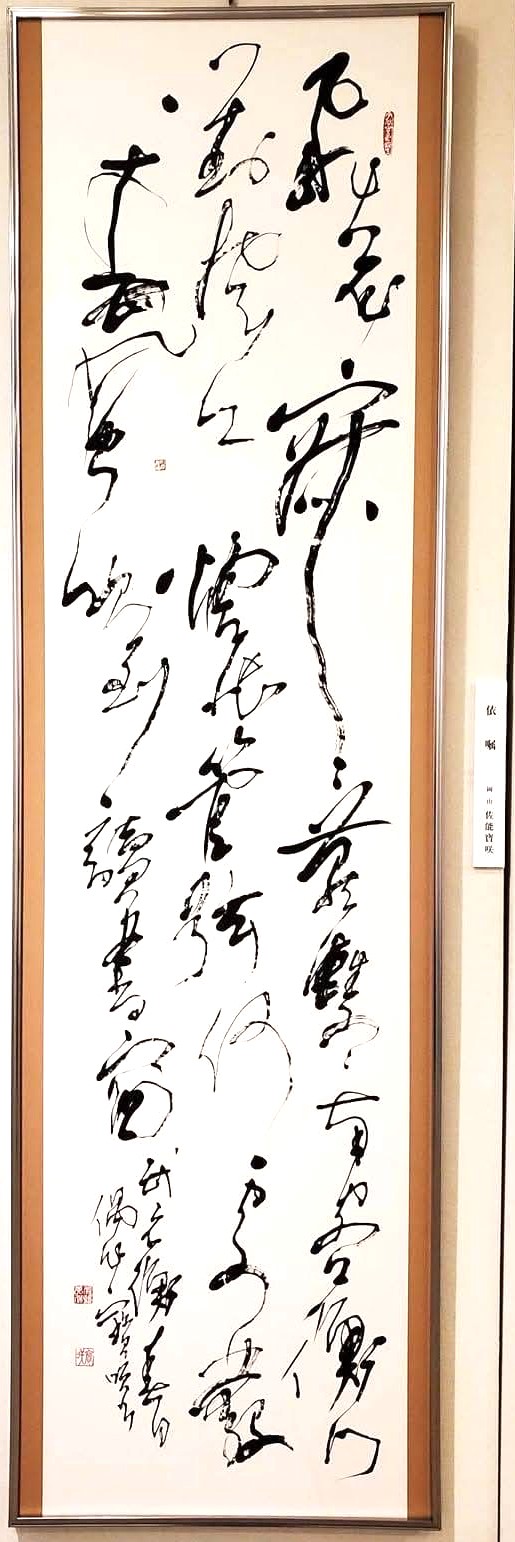 淡い茶色の額に収められた春日偶作の縦長の書作品
